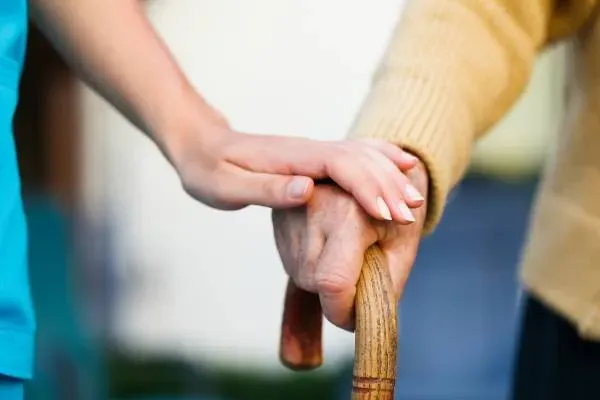 Gros plan sur une main posée avec bienveillance sur celle d'une personne âgée tenant une canne.