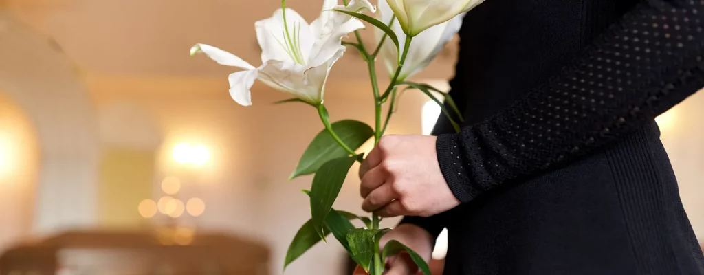 Une personne vêtue de noir tient un bouquet de lys blancs dans ses mains.