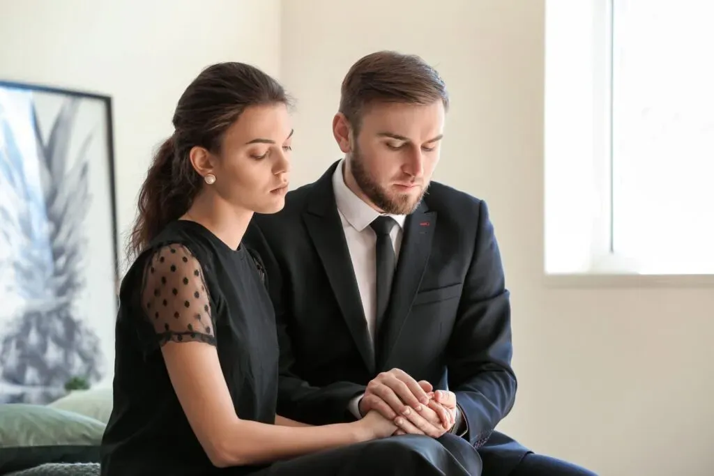 Un homme et une femme habillés en noir se tiennent la main dans un moment de recueillement.