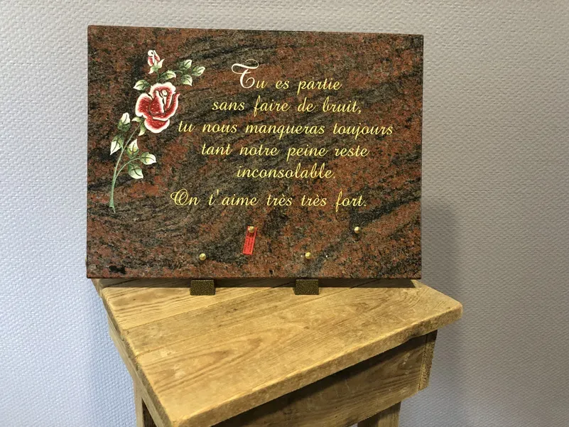 Plaque funéraire en granite rose posée sur un meuble en bois et gravée d'un texte d'hommage.